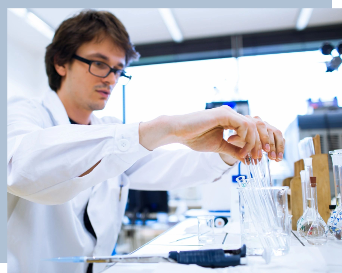 A man in white lab coat working with glass.